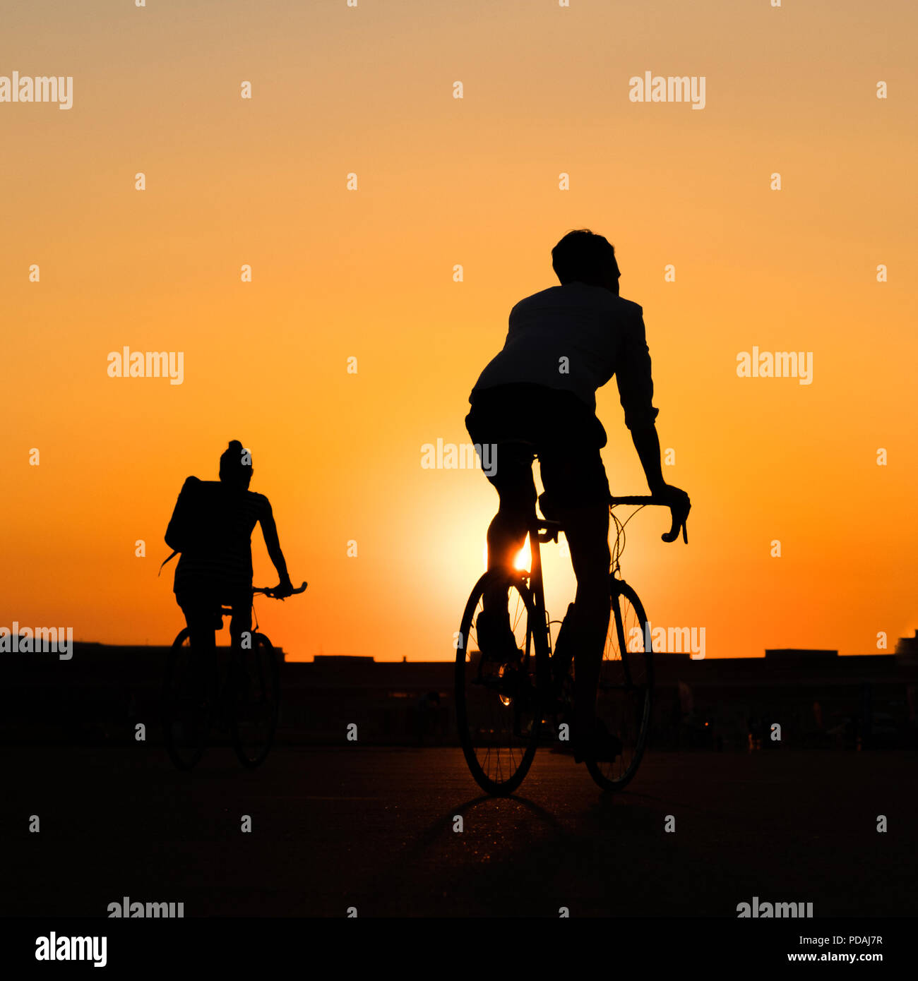 silhouette of young man riding racing bicycle with sunset sky background - Stock Photo