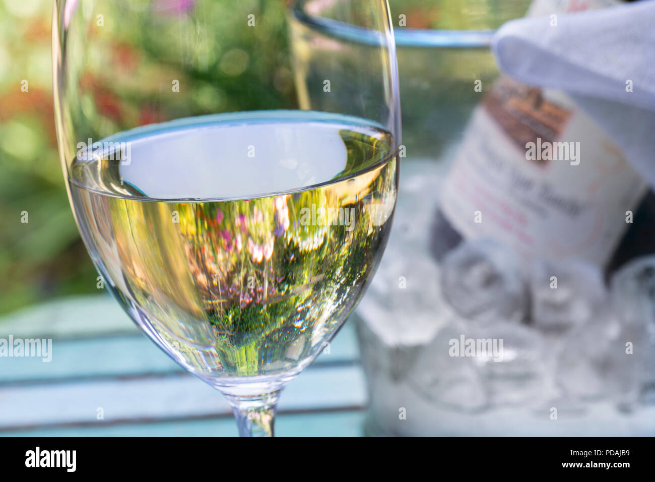 white wine chilled on alfresco terrace table with bottle and ice cubes wine cooler behind in floral garden summer tasting lifestyle situation Stock Photo