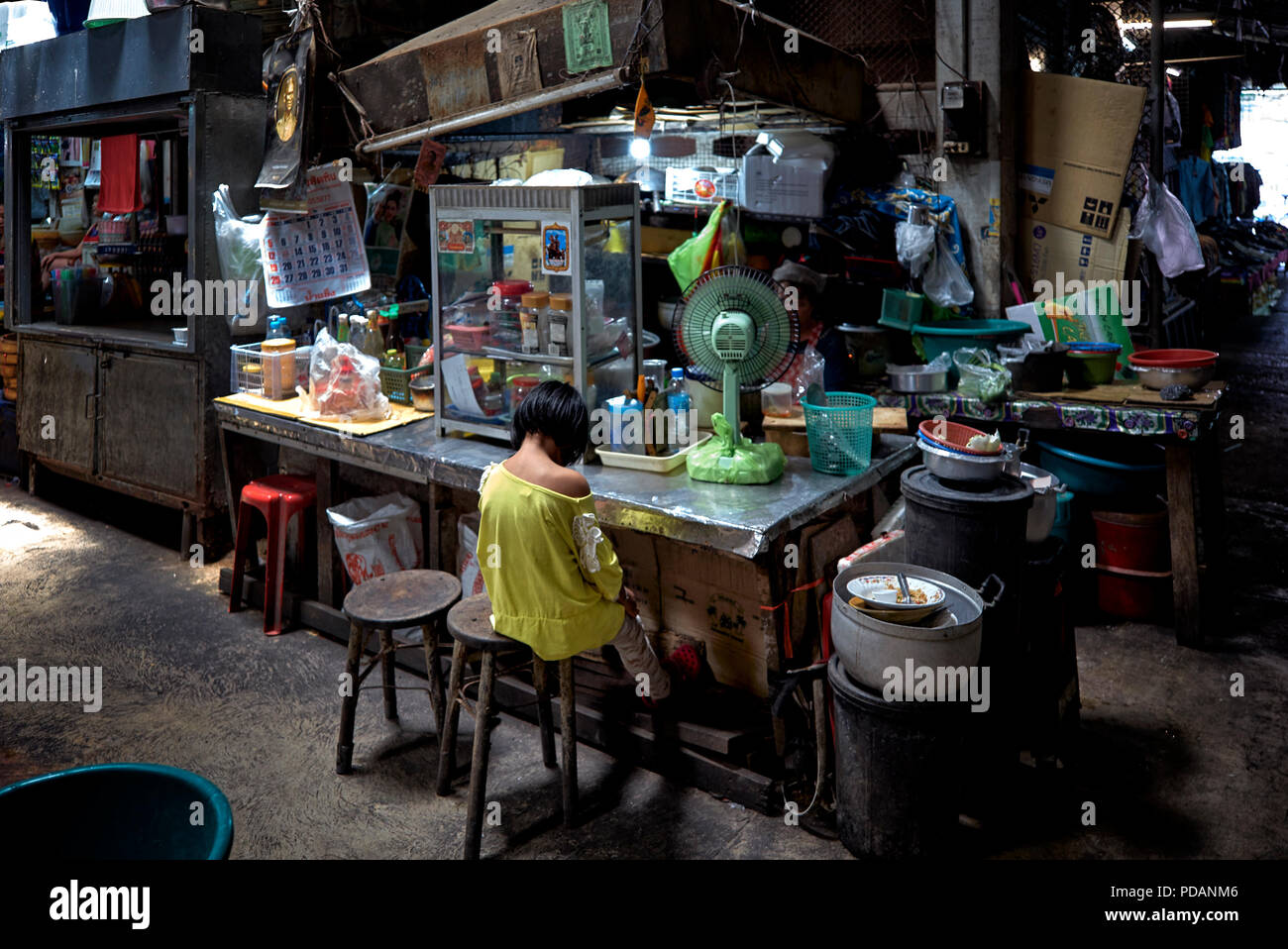 Child alone at a dimly lit Thailand market back street stall. Stock Photo