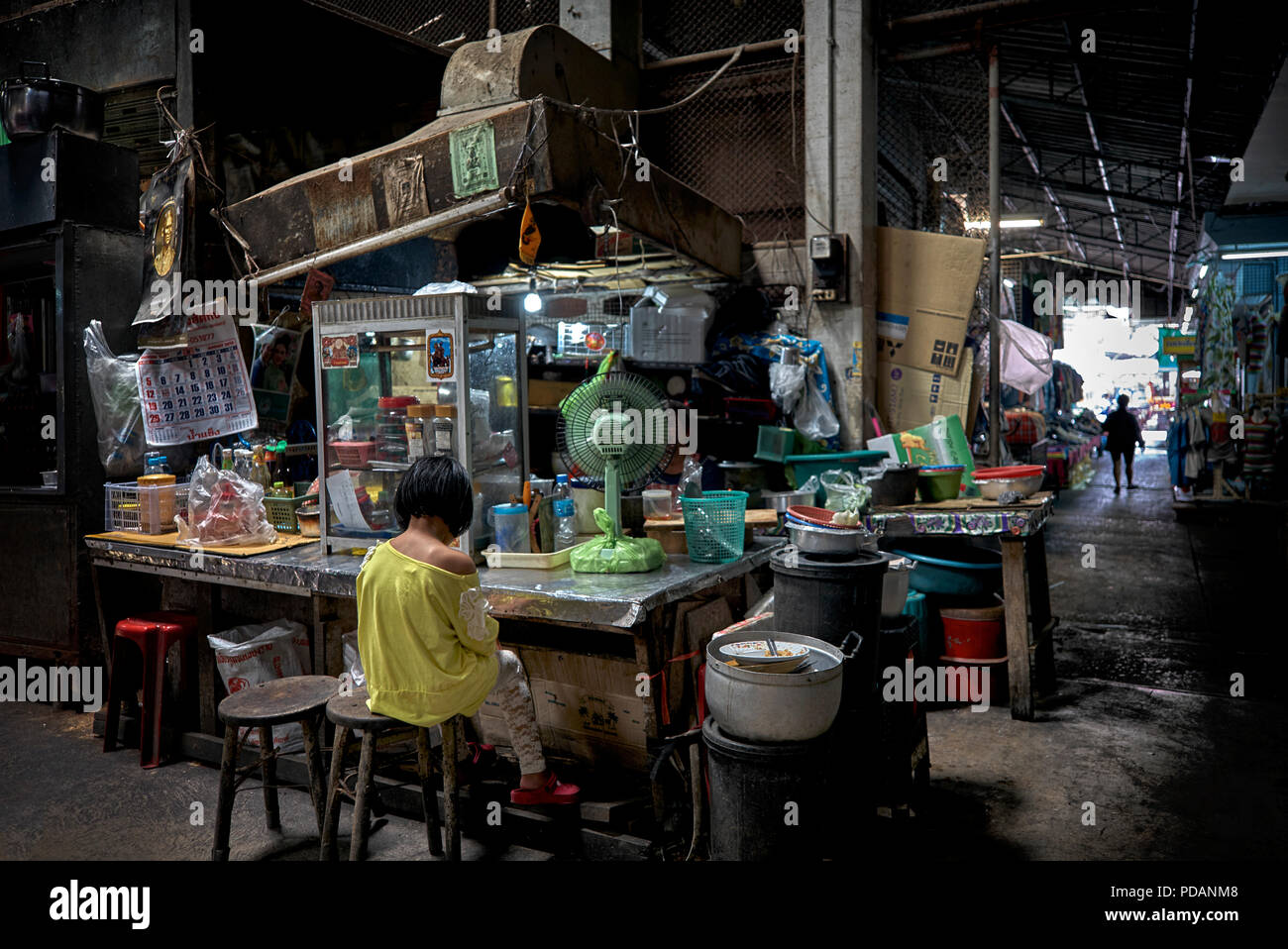 Child alone at a dimly lit Thailand market back street stall. Stock Photo