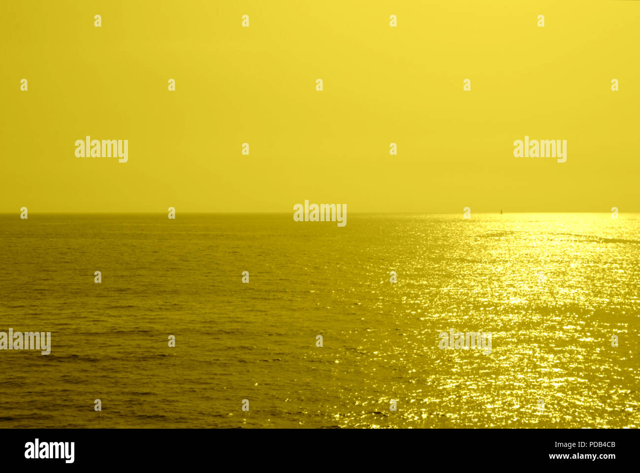 Summer minimalist background, yellow monochromatic glittering sunset on the sea, with the sun coming down to the horizon Stock Photo