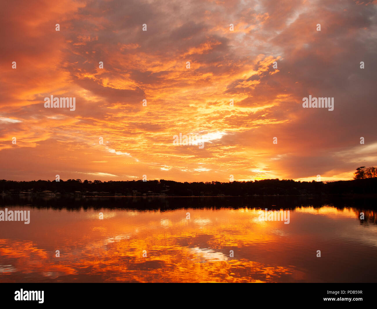A huge Orange stratocumulus cloudy sunrise seascape, over sea water with water reflections. Queensland, Australia. Stock Photo