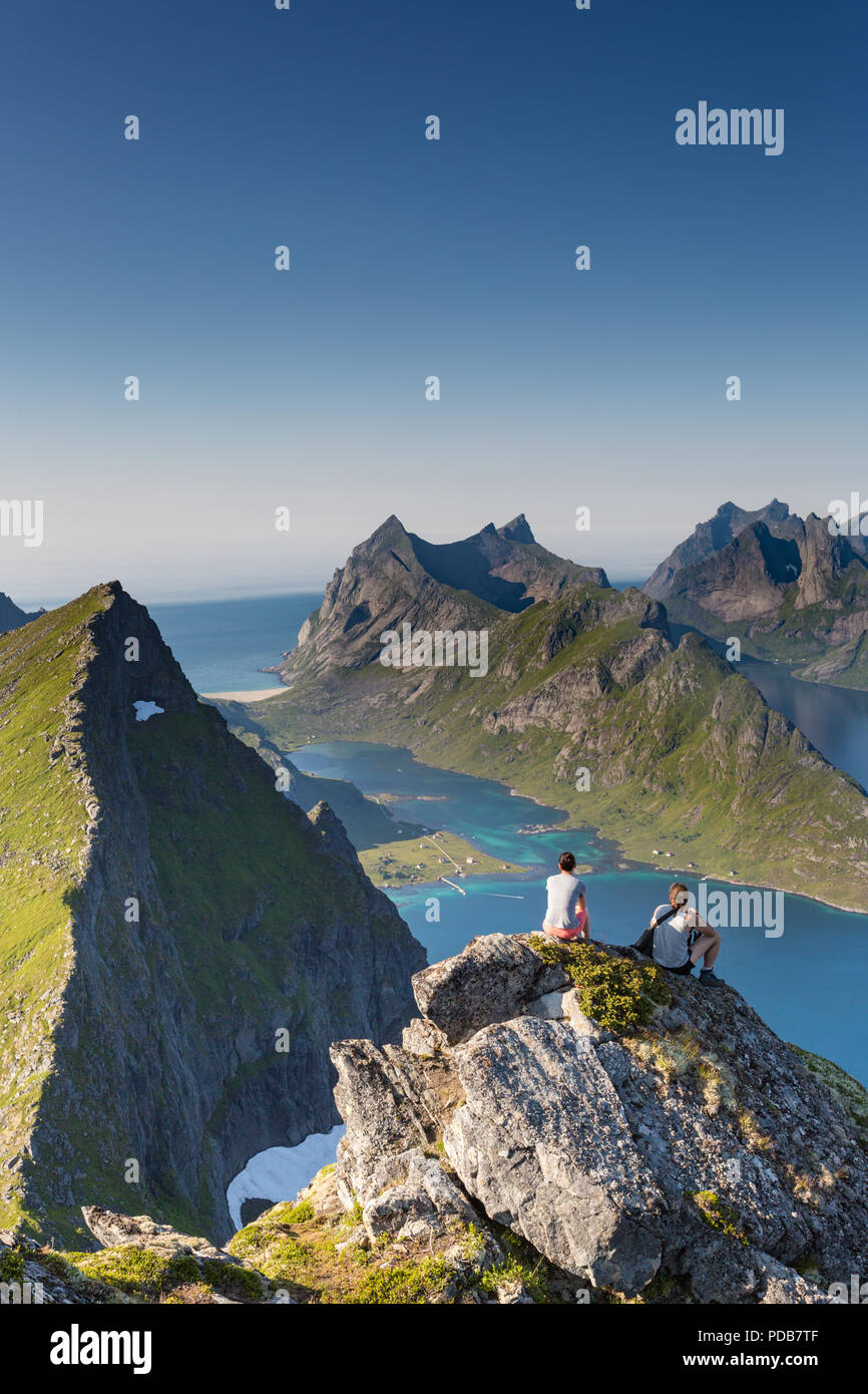 Two hikers rest after reaching the summit of Munkan, a classic hike in the Lofoten Islands. Stock Photo