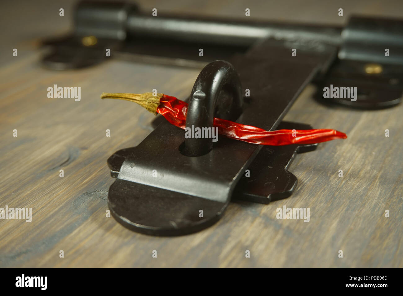 Old metal hasp and staple lock with a red hot chili pepper threaded through it in a conceptual image on a wood background Stock Photo