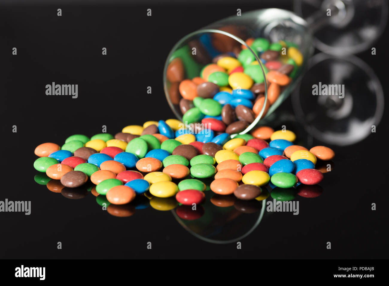 Champagne flute fallen over and spilling contents of multi colored m&m candies over black background Stock Photo