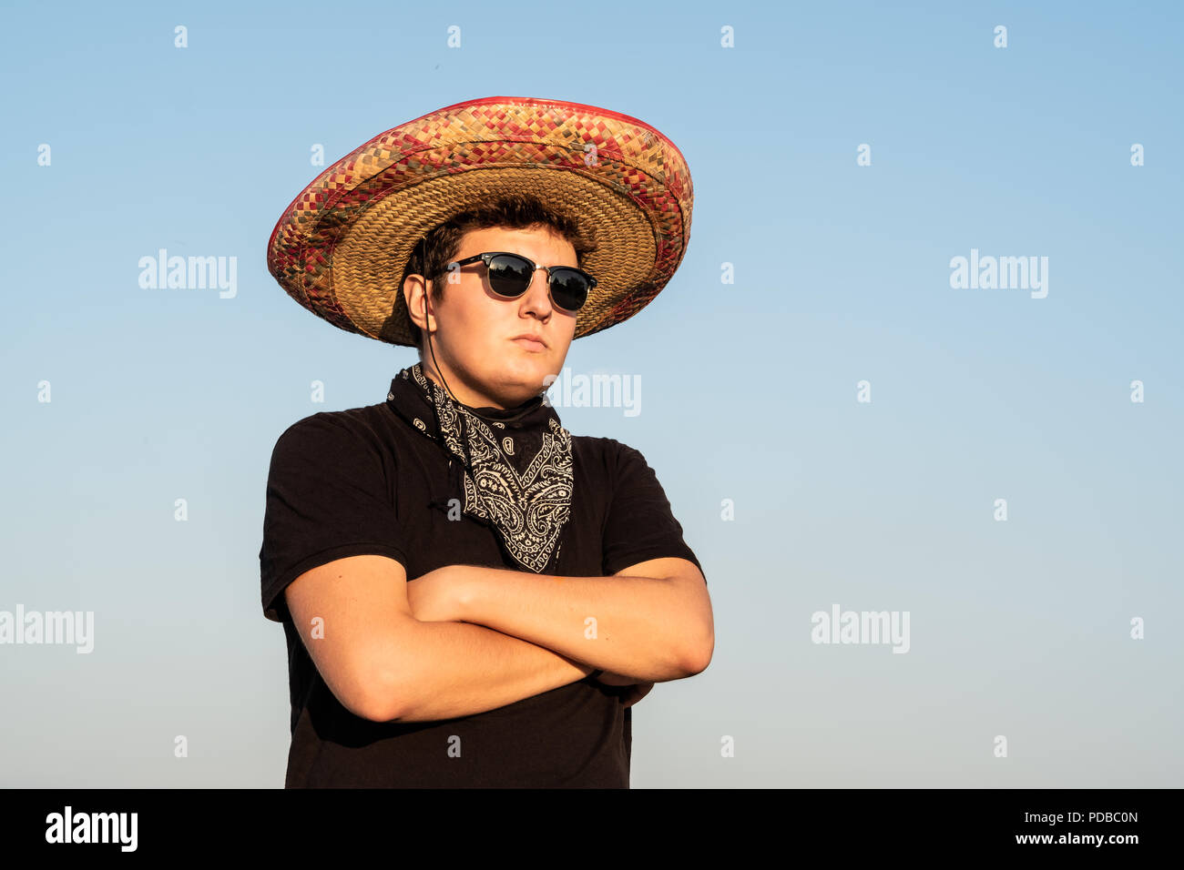 Young male person in sombrero and sunglasses in clear sky background. Mexico independence festive concept of man wearing national mexican hat and west Stock Photo