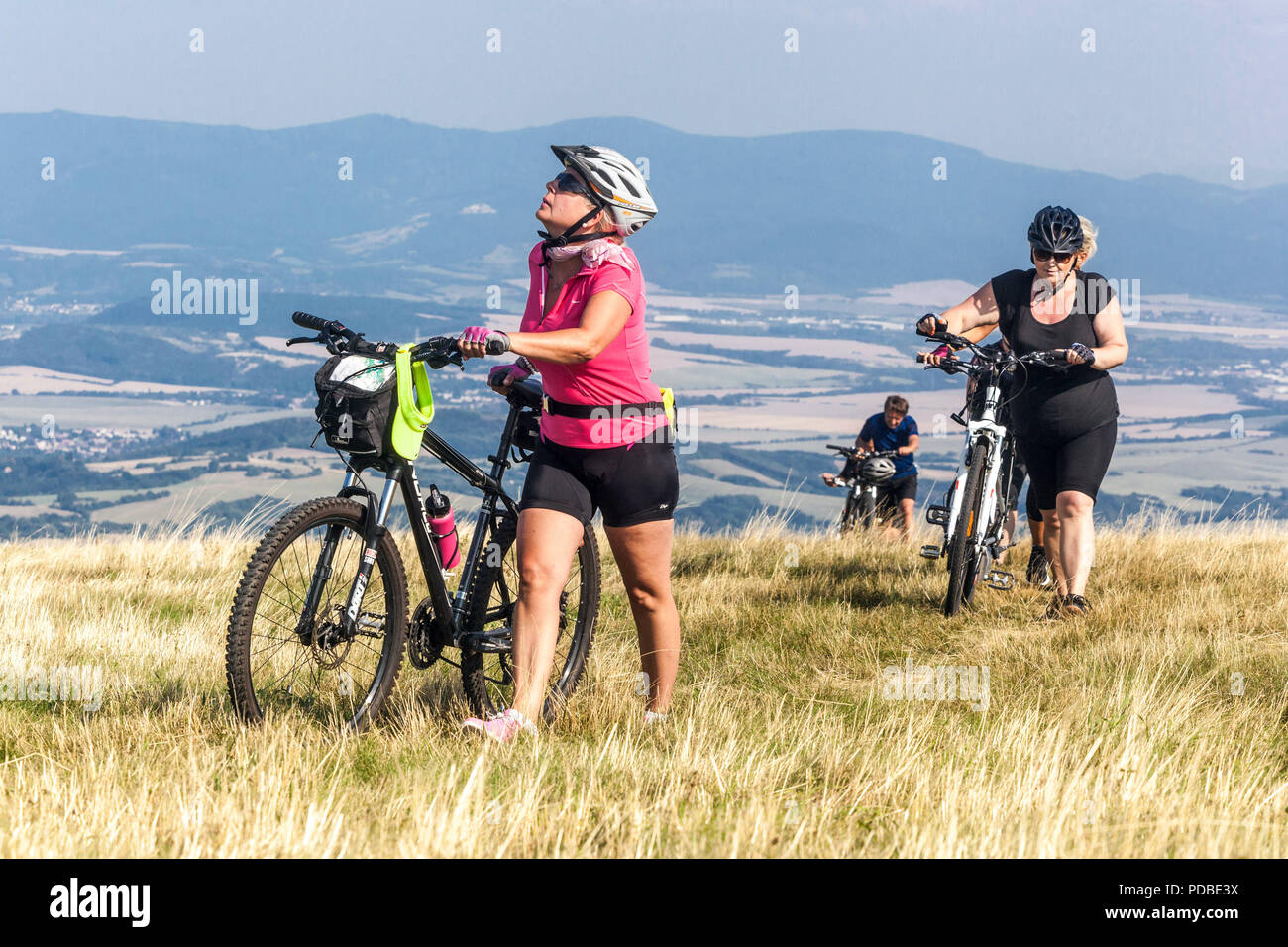 Bikers cycling on a mountain trail, Velka Javorina hill, Czech Slovak border in White Carpathians Women pushing an uphill Stock Photo