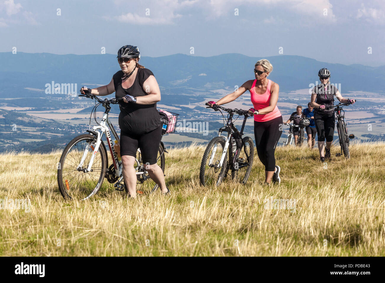 Women ride a bike, Bikers cycling on a mountain trail, Velka Javorina mountain, Czech Slovak border in White Carpathians Women pushing an uphill Stock Photo