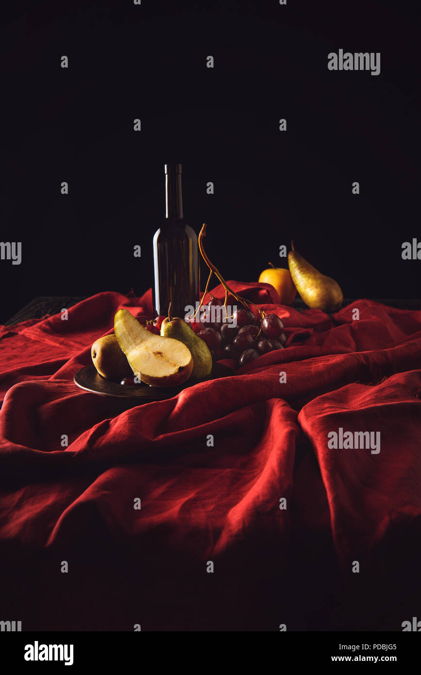 still life with different fruits and wine bottle on red drapery on black Stock Photo