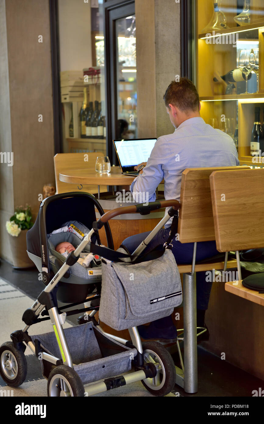 Man working on a computer laptop in public cafe with child in pram next to him Stock Photo