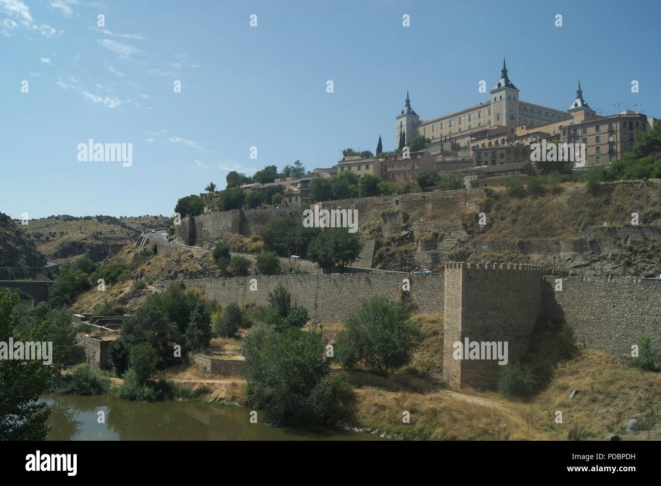 View of the historic Alcazar at the ancient Spanish city of Toledo. Defensive walls line the riverbank and the old monument stands proud on the hill. Stock Photo