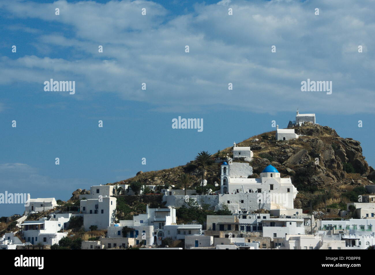 View of the old town on the idyllic Greek island of Ios.  Three small chapels on a steep hill above the  traditional village. Blue sky and copy space. Stock Photo