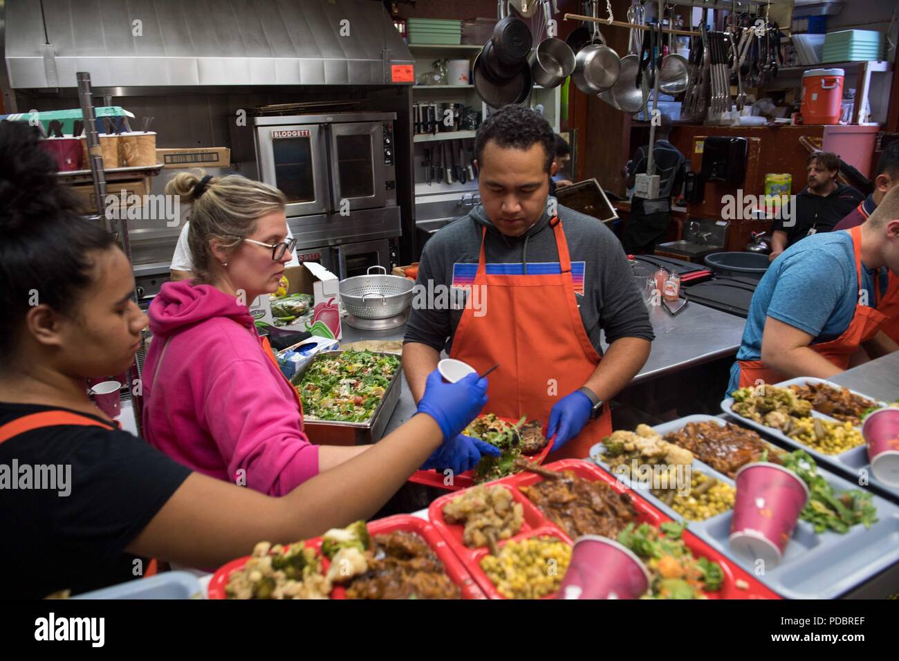 180803-N-DA737-0186 SEATTLE (Aug. 3, 2018) Hospital Corpsman 1st Class Jonathan Faletoi (right), assigned to Naval Hospital Bremerton, prepares meals with his wife, Stephanie, (middle), and sister, Patricia, (left), at Bread of Life Mission during a Seattle Seafair Fleet Week community relations event. Seafair Fleet Week is an annual celebration of the sea services wherein Sailors, Marines and Coast Guard members from visiting U.S. Navy and Coast Guard ships and ships from Canada make the city a port of call. (U.S. Navy photo by Mass Communication Specialist 2nd Class Jonathan Jiang/Released) Stock Photo