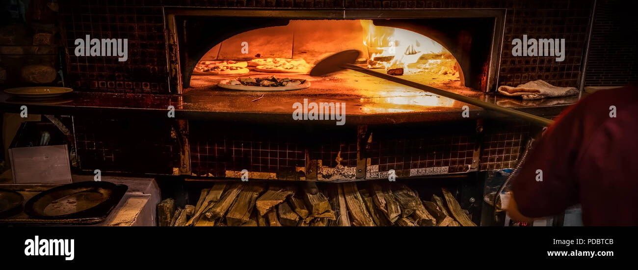 Pizza cooking in a wood fired pizza oven with plenty of fuel underneath. Stock Photo