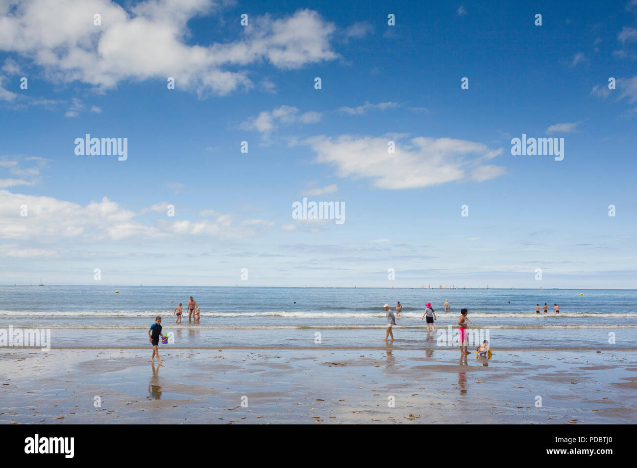 Holidaymakers on the shoreline of the expansive sandy beach at Deauville, Normandy, France with sailing boats on the horizon Stock Photo