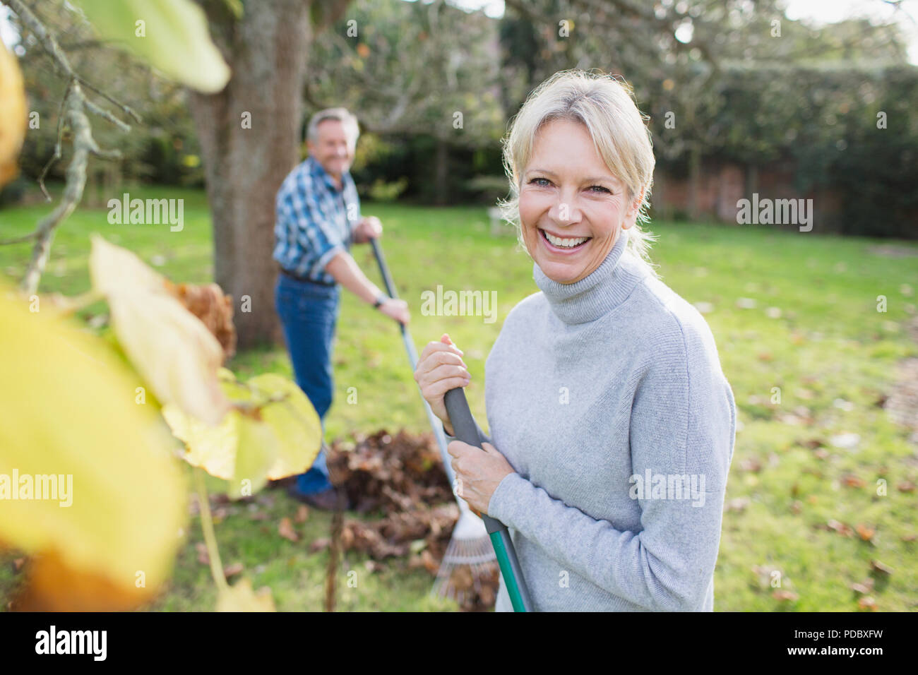 Portrait smiling, confident mature woman raking autumn leaves in backyard Stock Photo