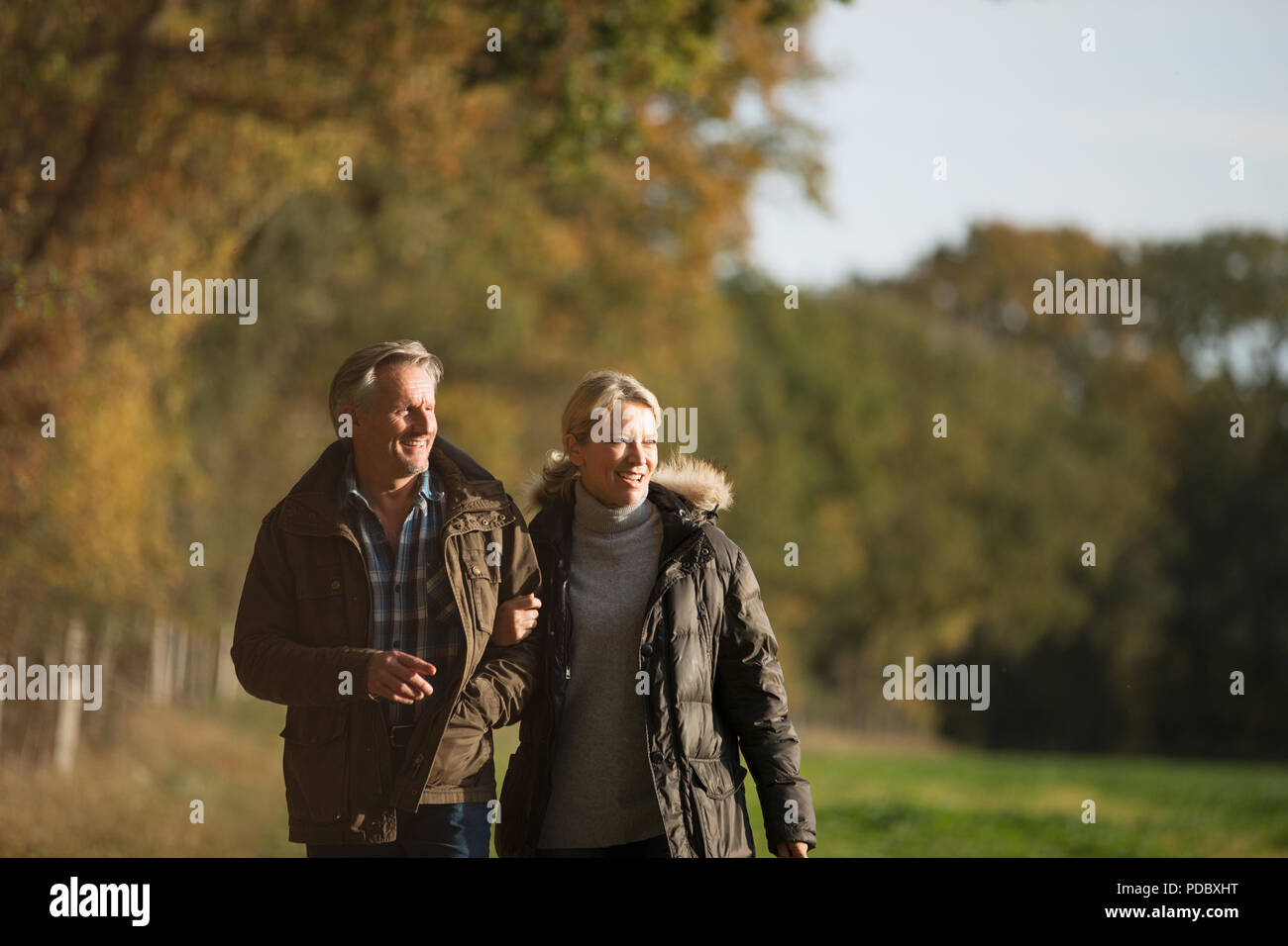 Mature couple walking arm in arm in sunny autumn park Stock Photo