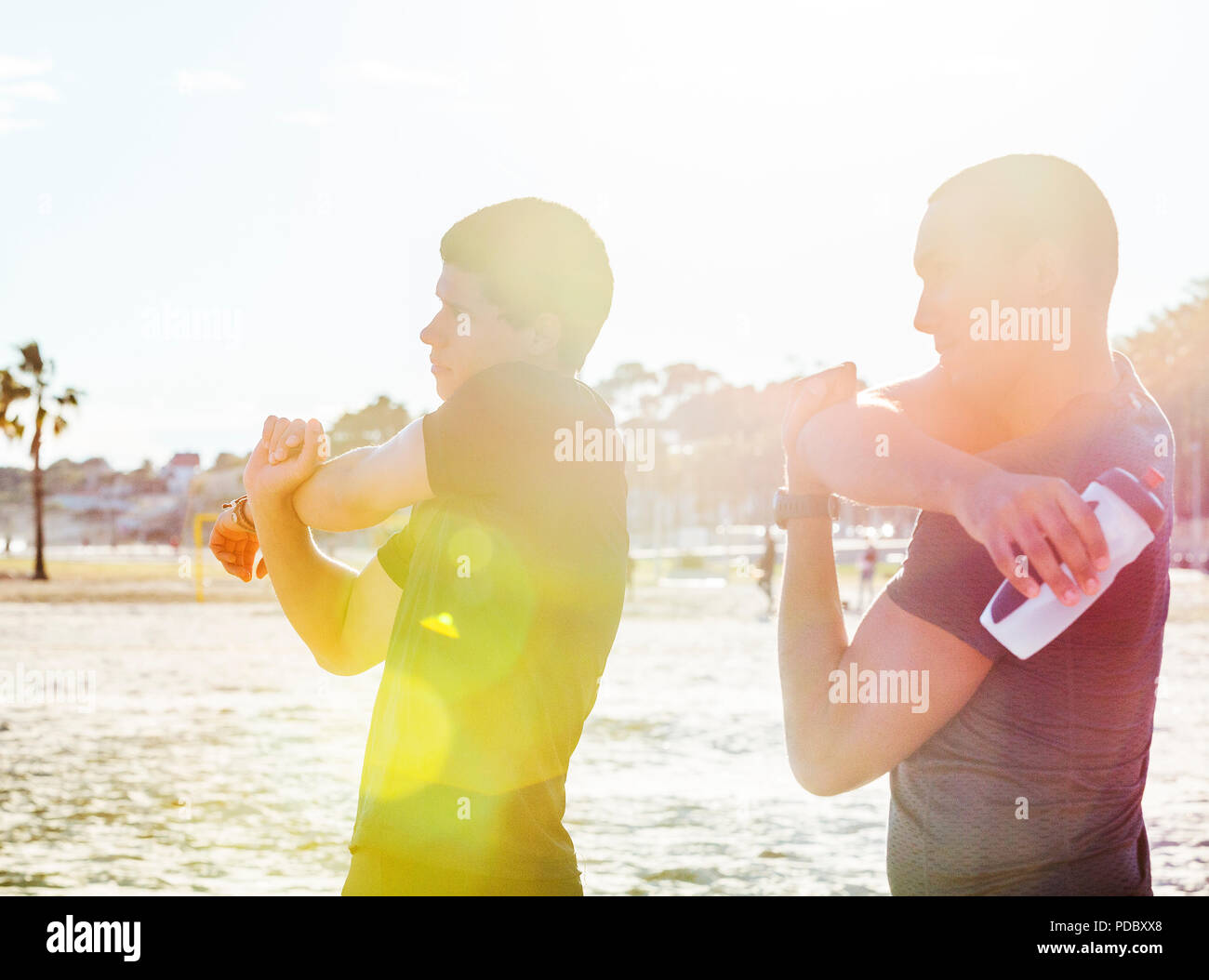 Male runners stretching arms on sunny beach Stock Photo