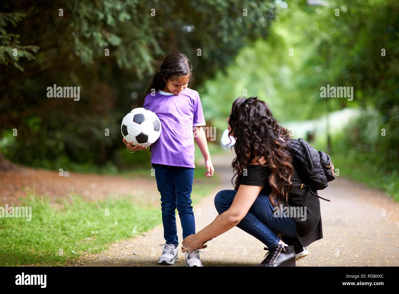 Mother tying shoelace of daughter holding soccer ball Stock Photo