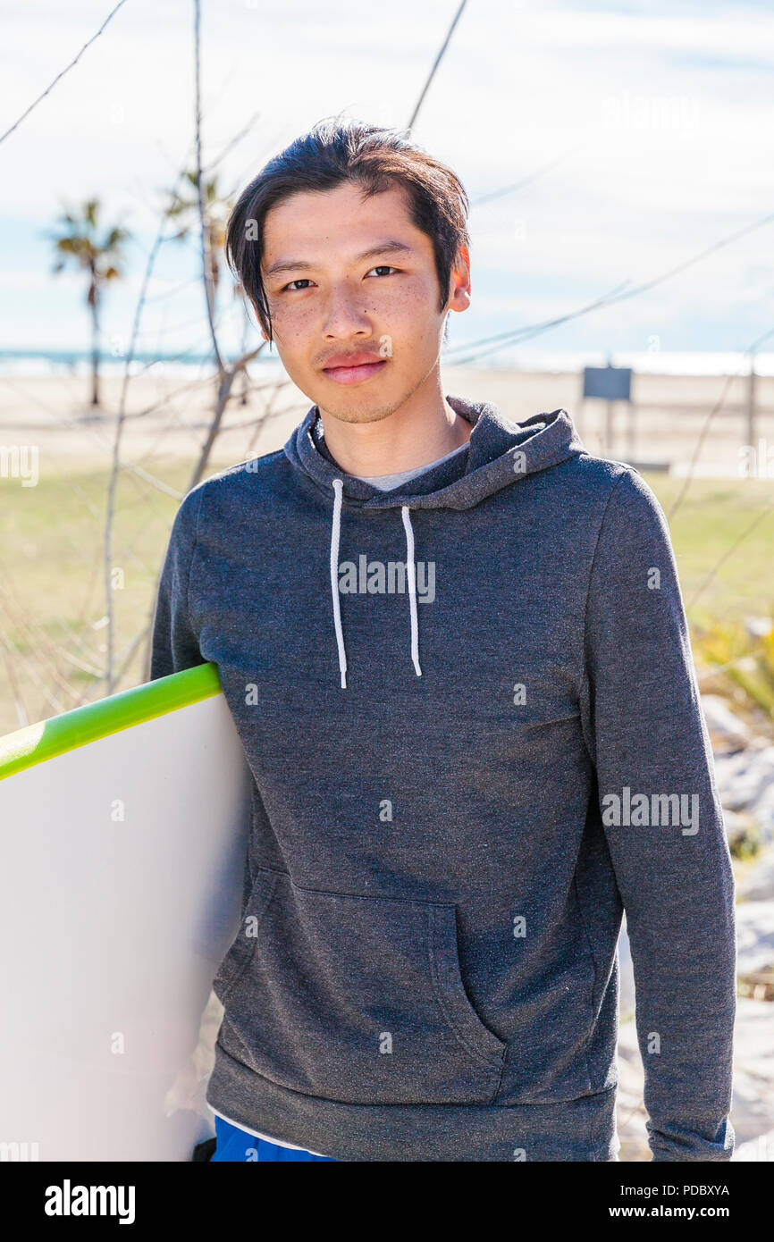 portrait of a surfer on the face of a sunscreen, wearing shorts and a black  T-shirt standing with a surfboard. yellow wooden background Stock Photo -  Alamy