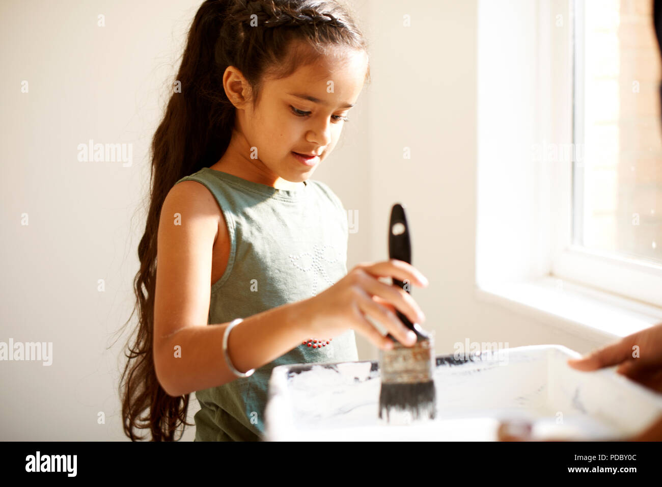 Girl painting, dipping paintbrush in tray Stock Photo