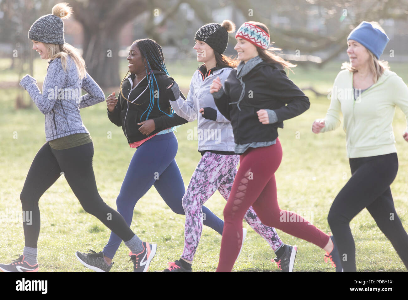 Smiling female runners running in sunny park Stock Photo