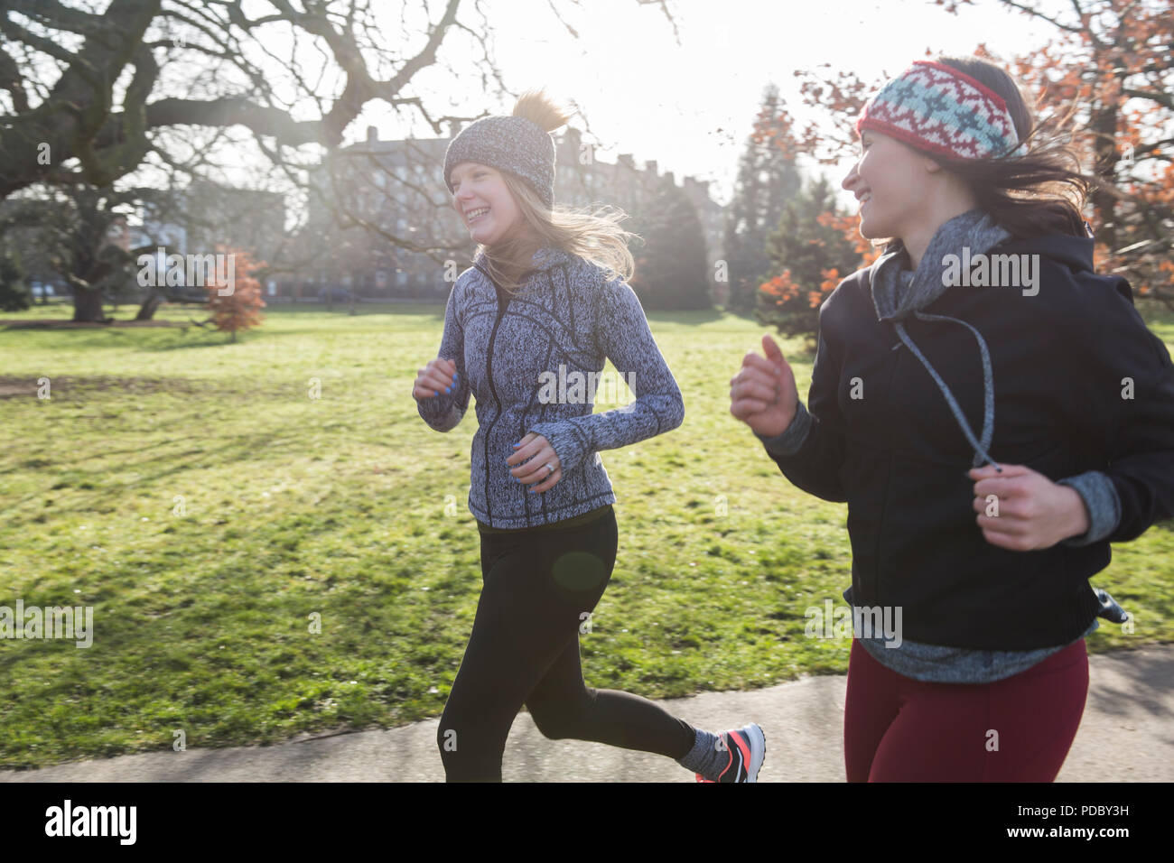 Smiling female runners running in sunny park Stock Photo