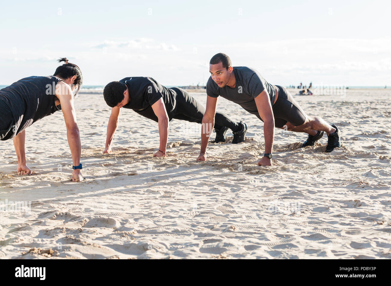 Men doing push-ups on sunny beach Stock Photo