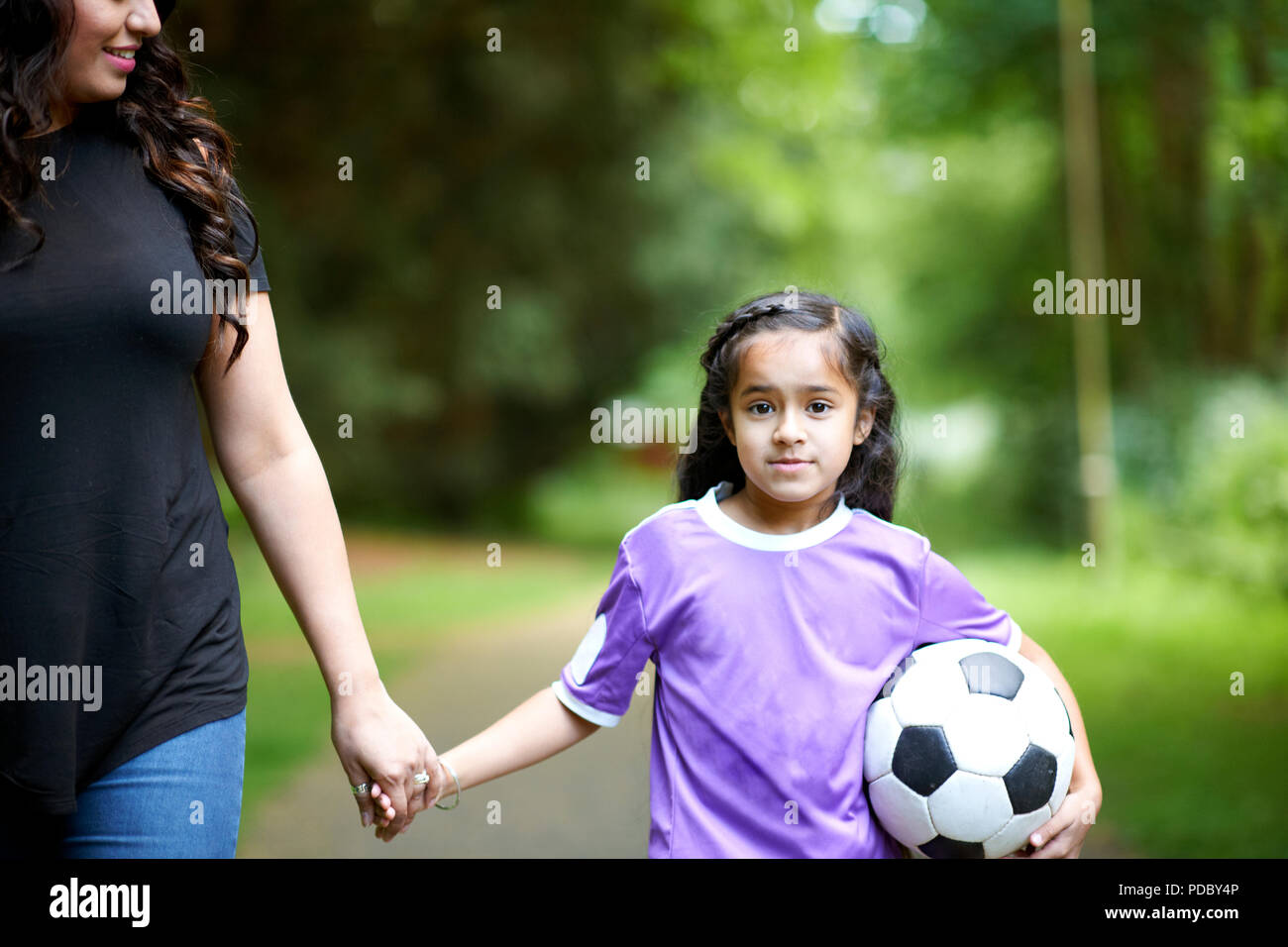 Portrait girl with soccer ball holding hands with mother Stock Photo