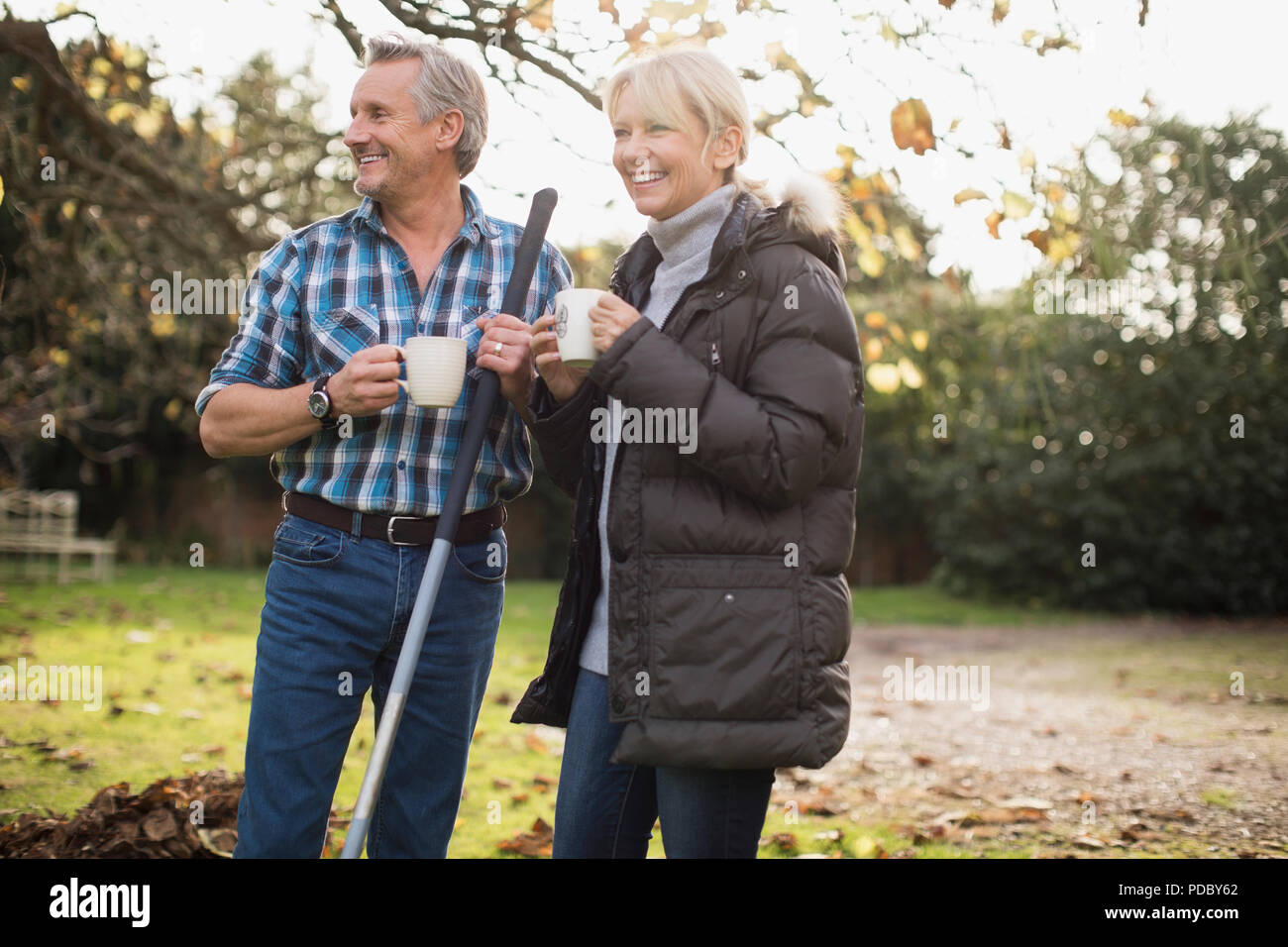 Mature couple drinking coffee and raking autumn leaves in backyard Stock Photo