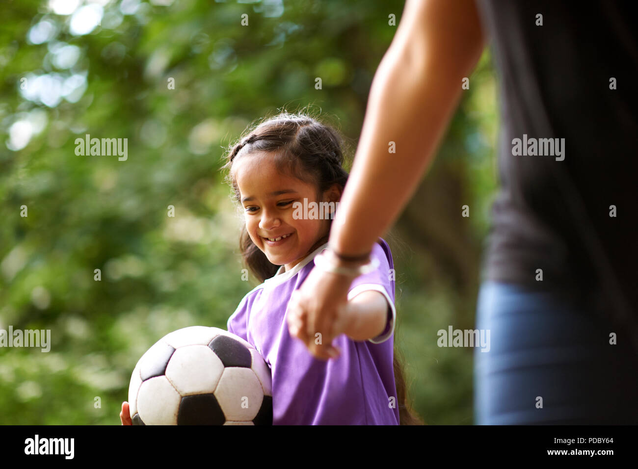 Smiling girl with soccer ball holding hands with mother Stock Photo