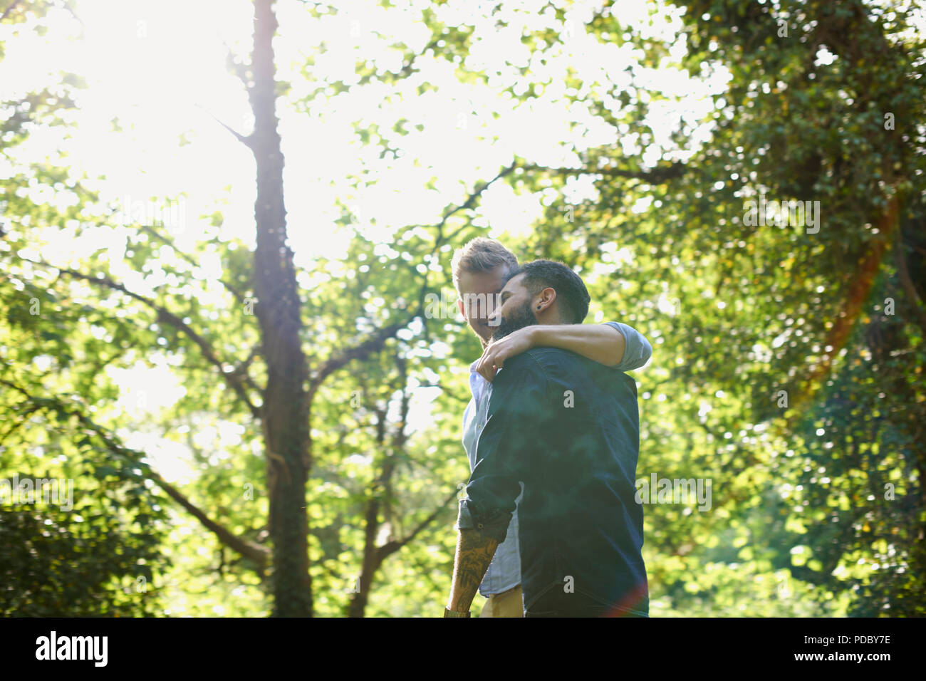 Affectionate gay couple hugging and walking in sunny park Stock Photo
