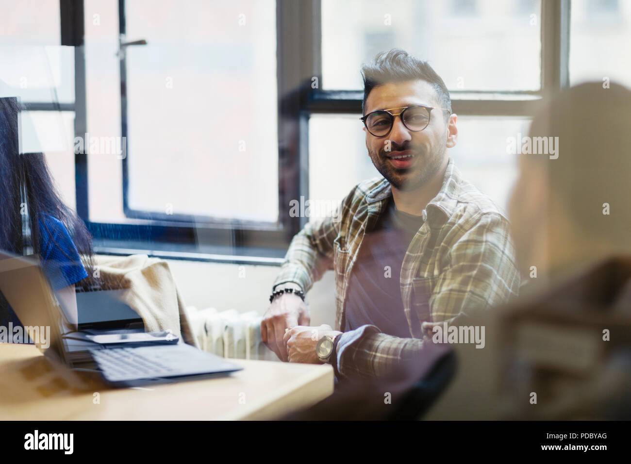 Smiling businessman at laptop talking with colleague in office meeting Stock Photo