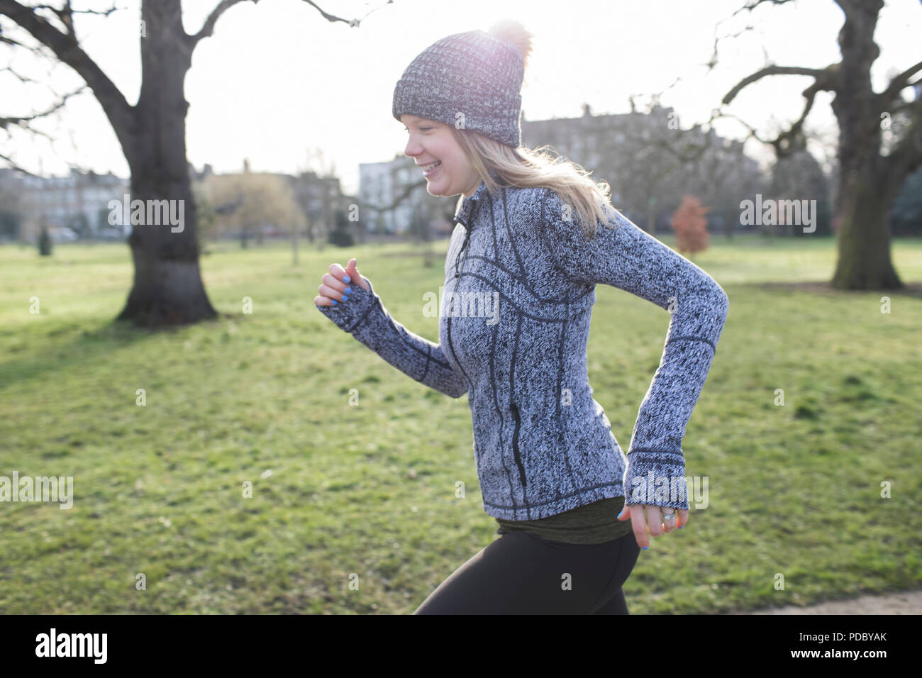 Smiling female runner running in sunny park Stock Photo