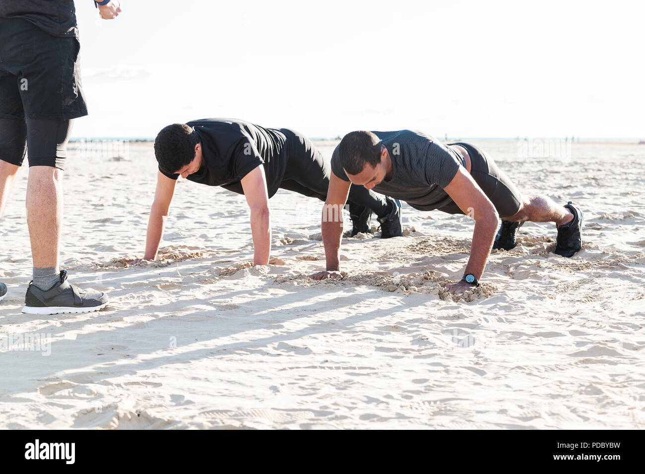 Men doing push-ups on sunny beach Stock Photo