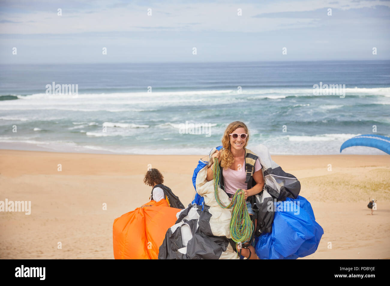 Portrait smiling, confident female paraglider with equipment on sunny ocean beach Stock Photo