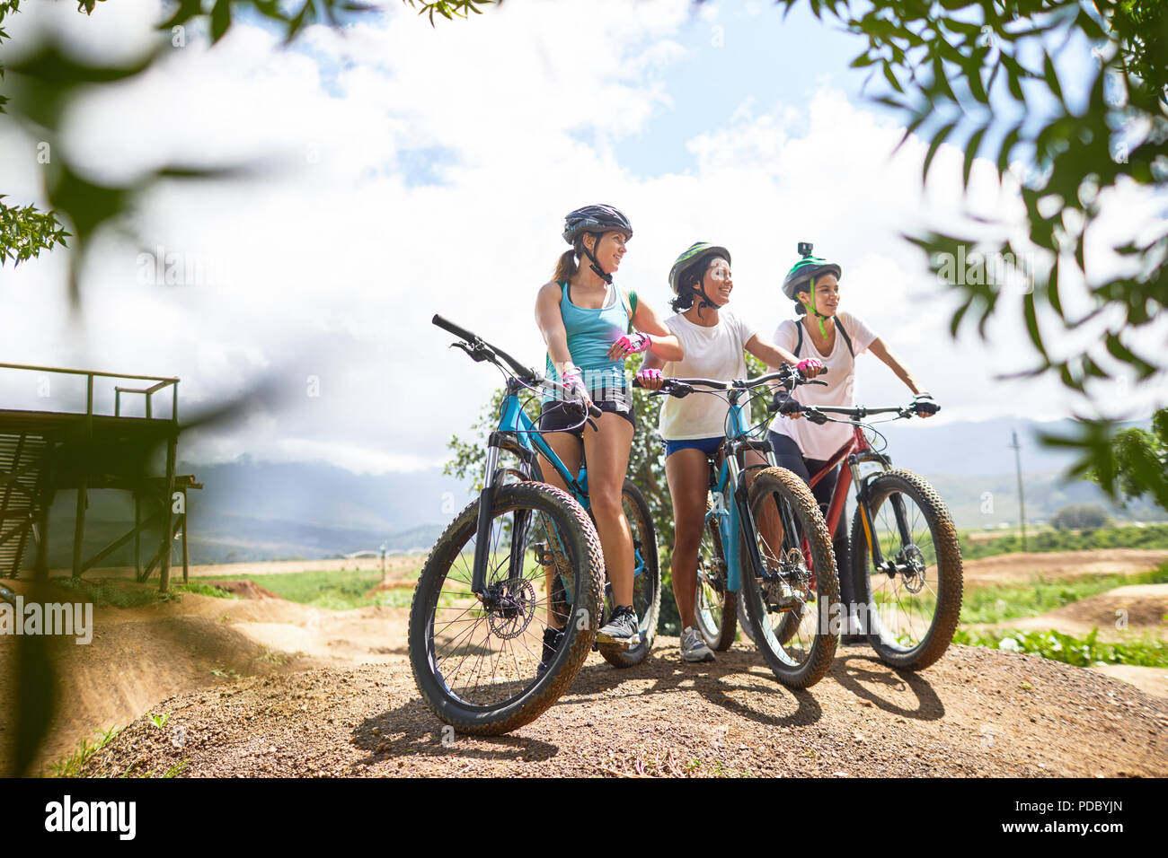 Women friends mountain biking on sunny obstacle course trail Stock Photo