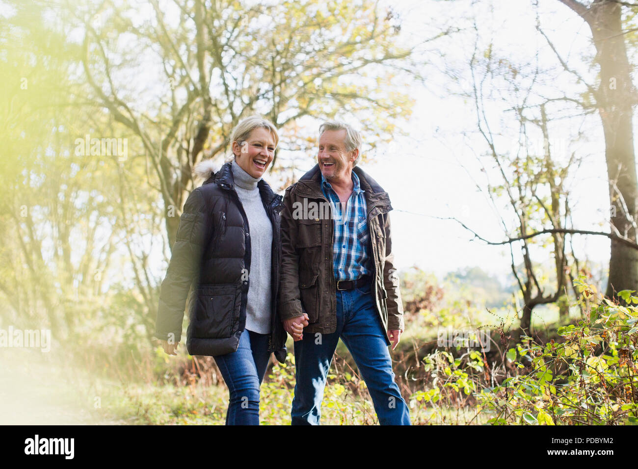 Happy mature couple holding hands, walking in sunny autumn park Stock Photo