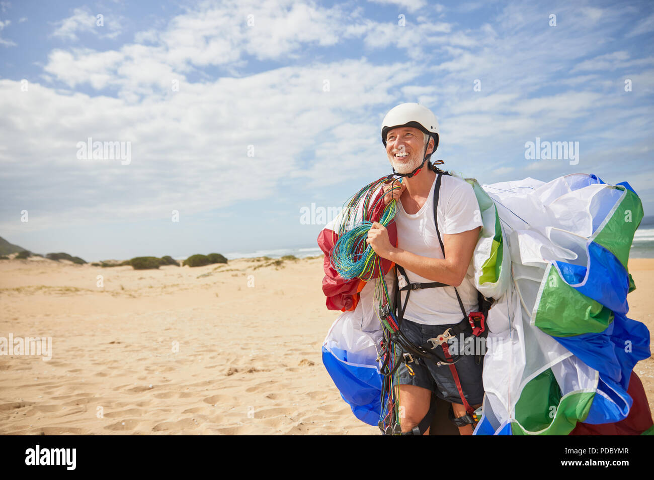 Smiling male paraglider carrying equipment and parachute on sunny beach Stock Photo