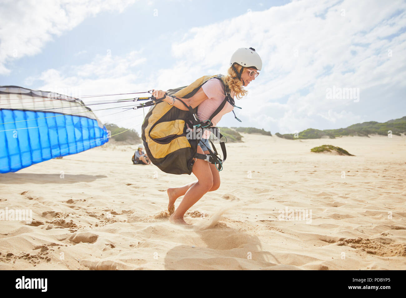 Female paraglider running with parachute on sunny beach Stock Photo