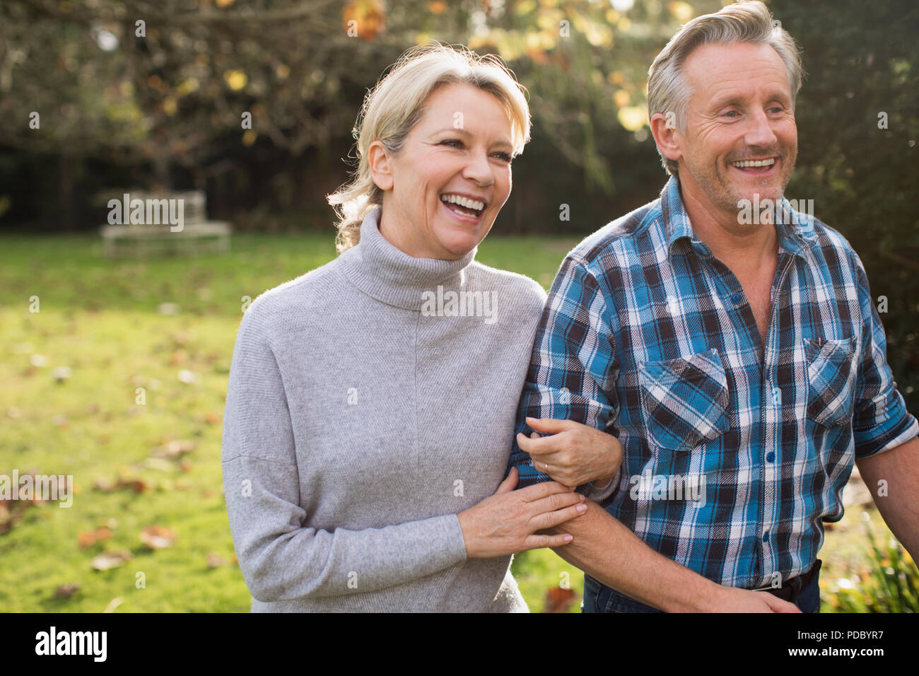 Happy, carefree mature couple walking arm in arm in sunny autumn park Stock Photo