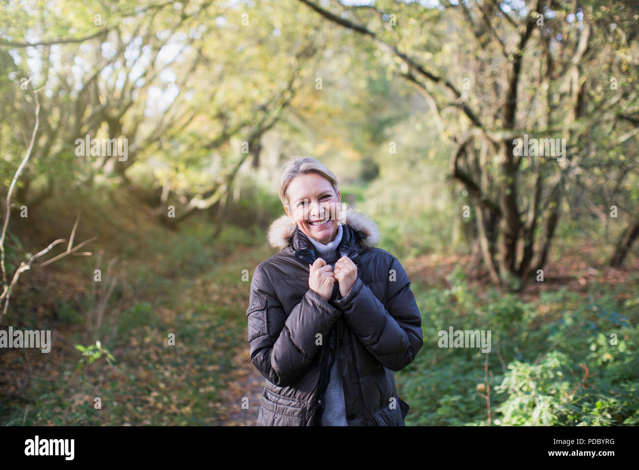 Portrait confident mature woman in parka in sunny autumn woods Stock Photo