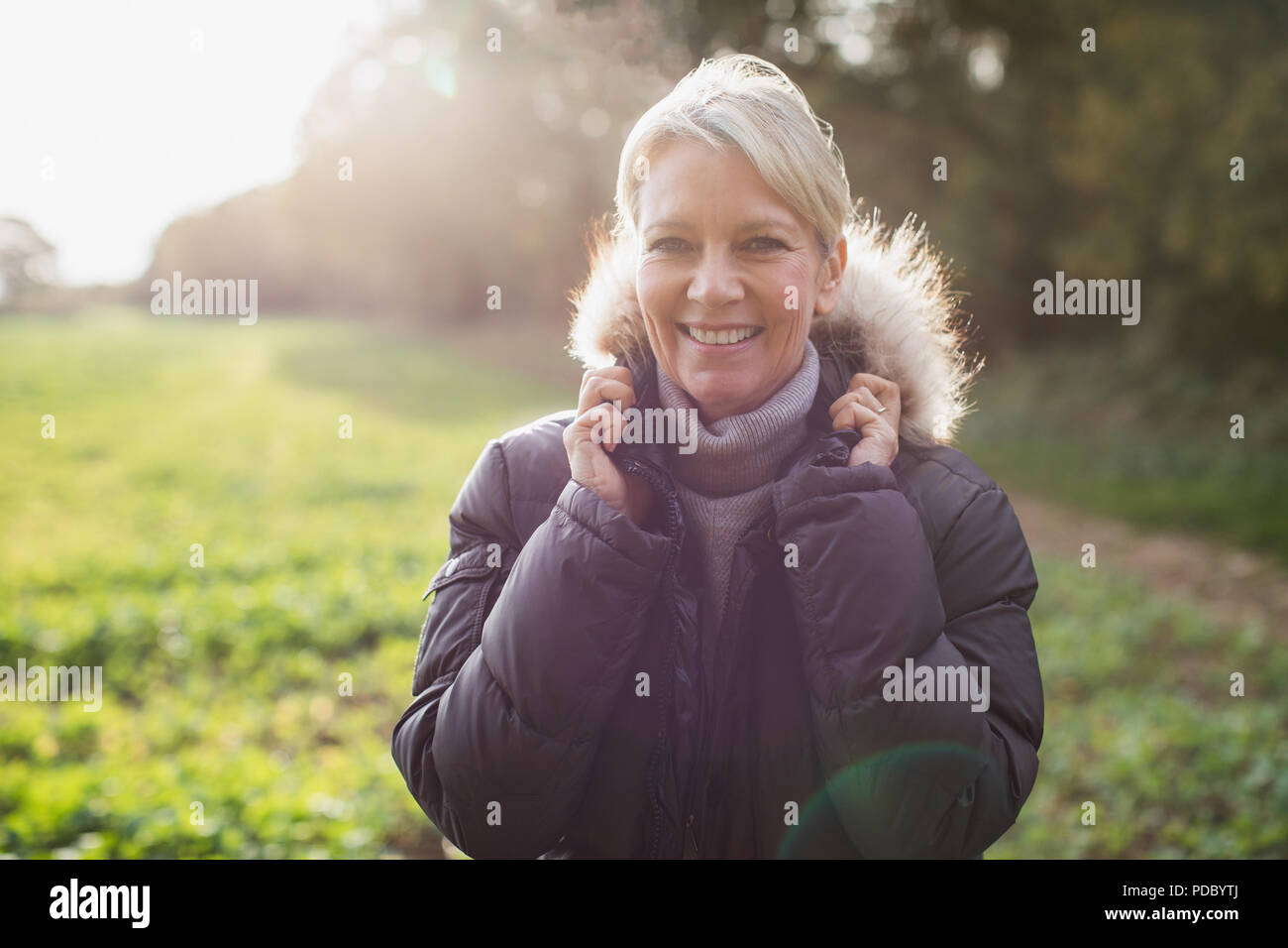 Portrait smiling, confident mature woman in parka in sunny park Stock Photo