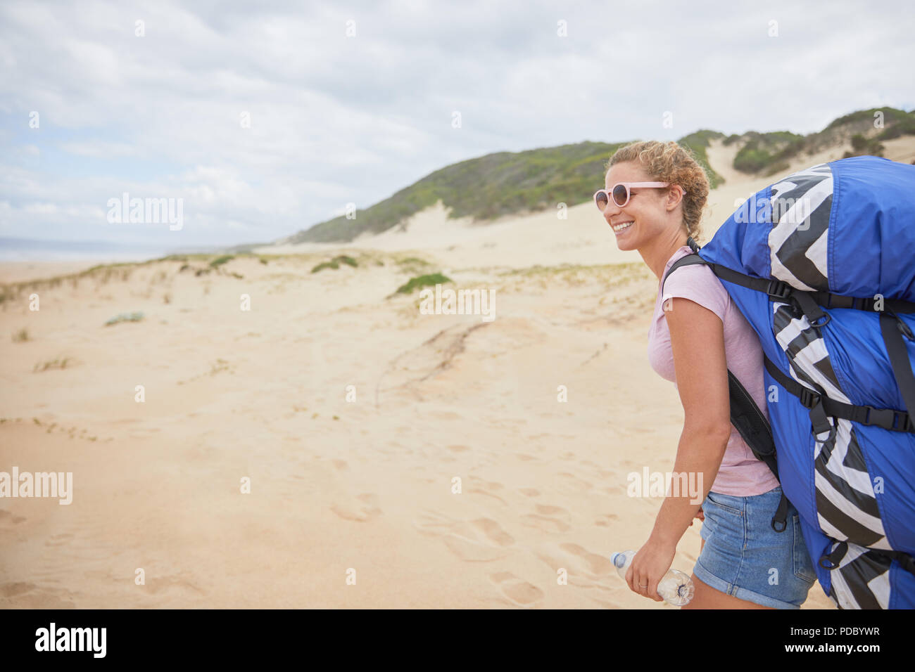 Smiling female paraglider with parachute backpack on beach Stock Photo