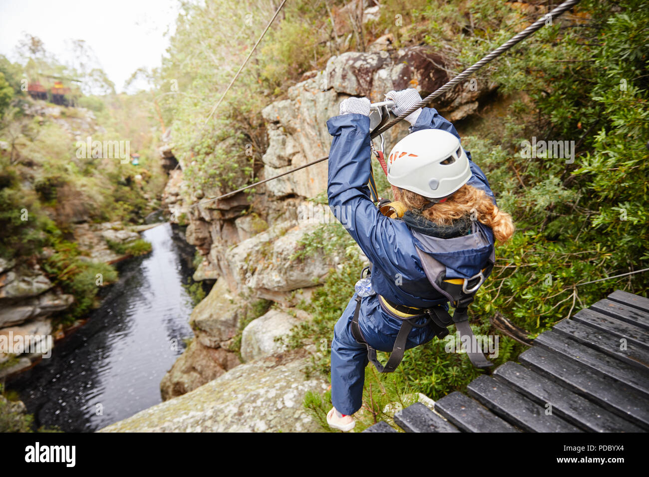 Woman zip lining over pond in woods Stock Photo