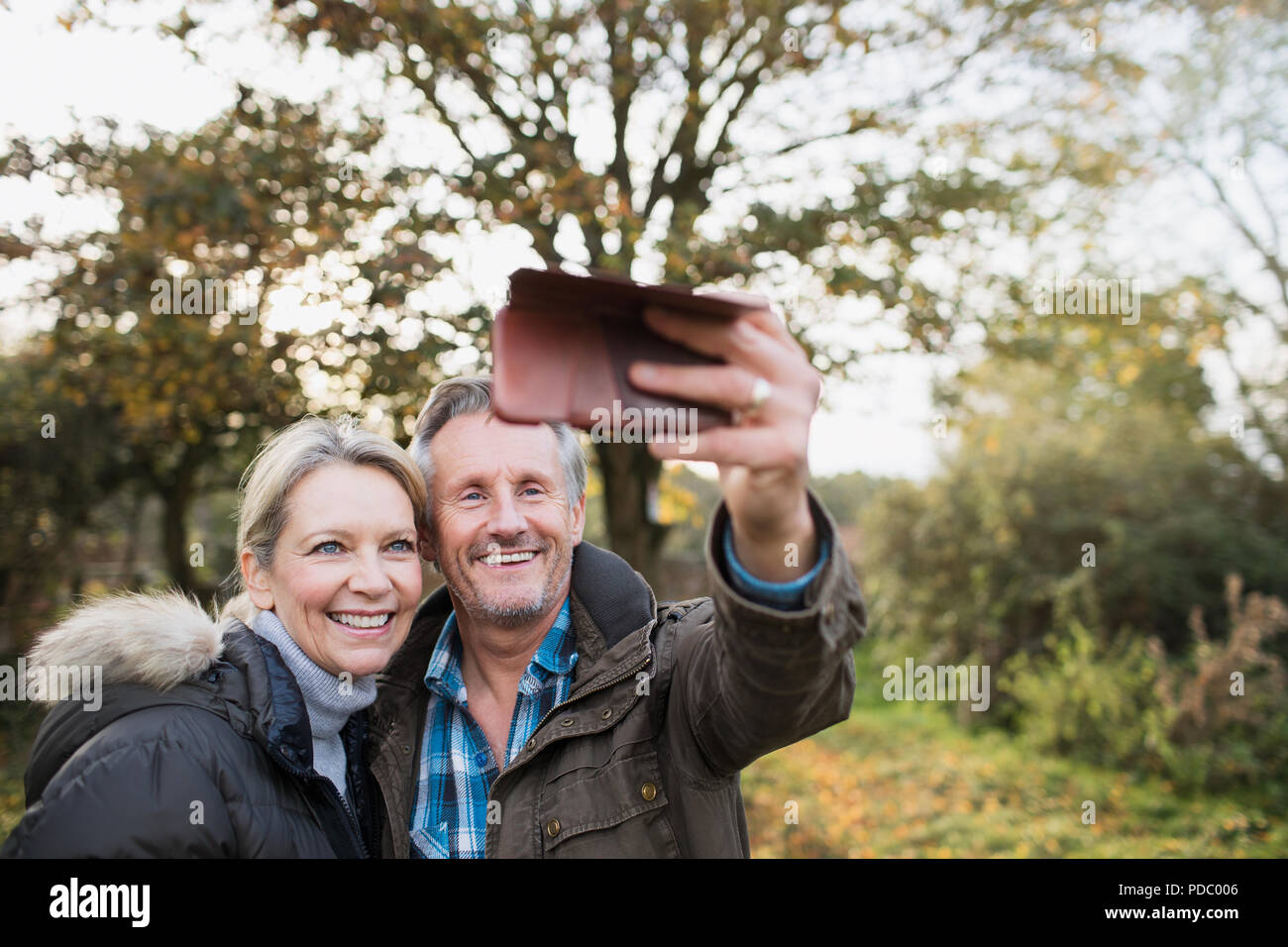Happy mature couple taking selfie with camera phone in autumn woods Stock Photo