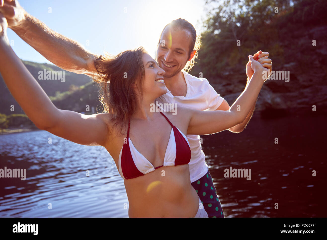 Happy, carefree couple holding hands at sunny summer lake Stock Photo
