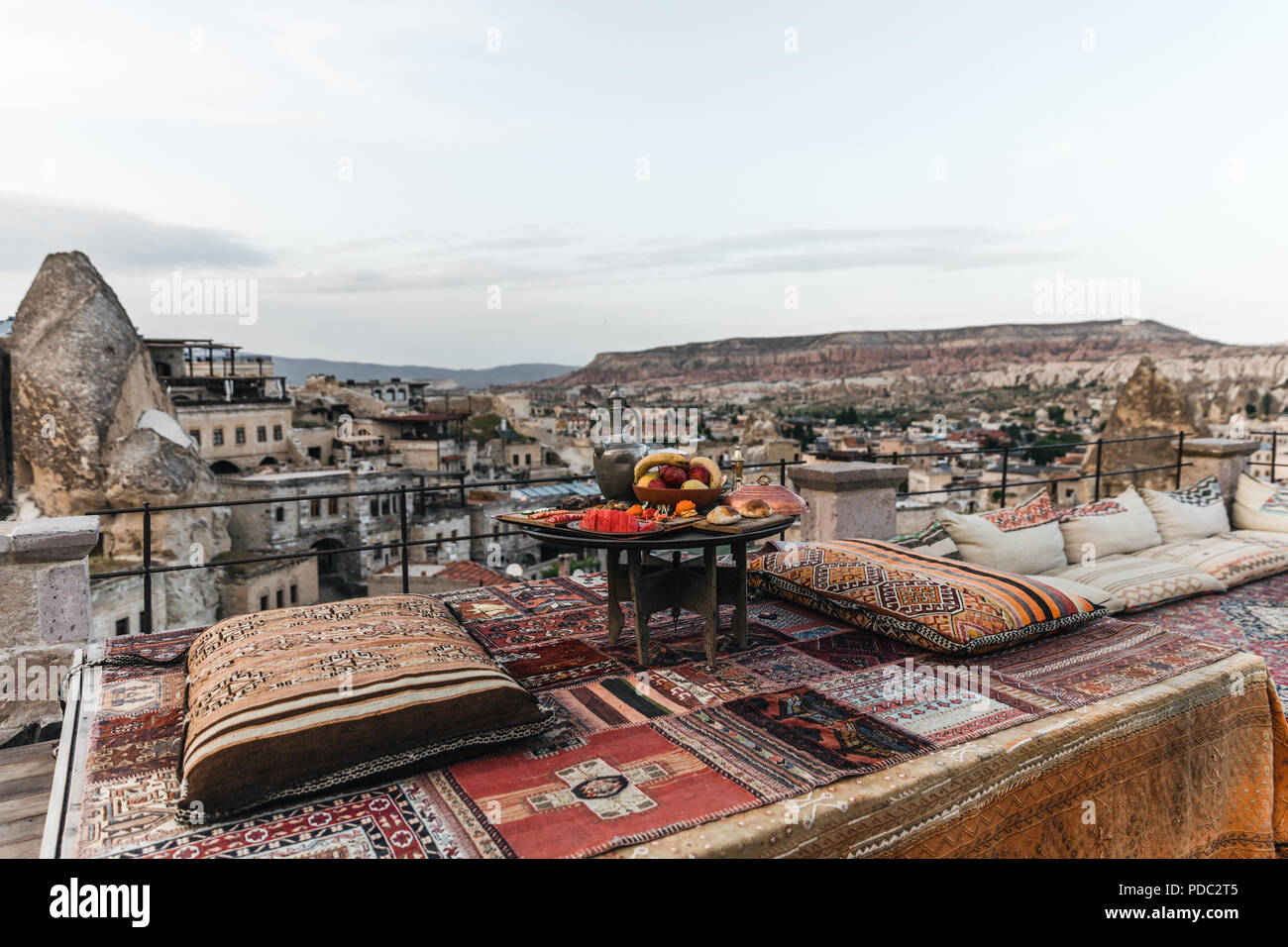 round table, traditional pillows and turkish carpet on terrace and beautiful view of traditional architecture and rocks in cappadocia, turkey Stock Photo