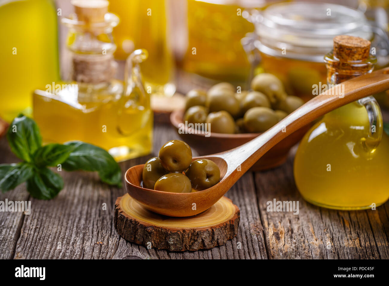 Pickled green olives in wooden spoon and olive oil in rustic bottles ...