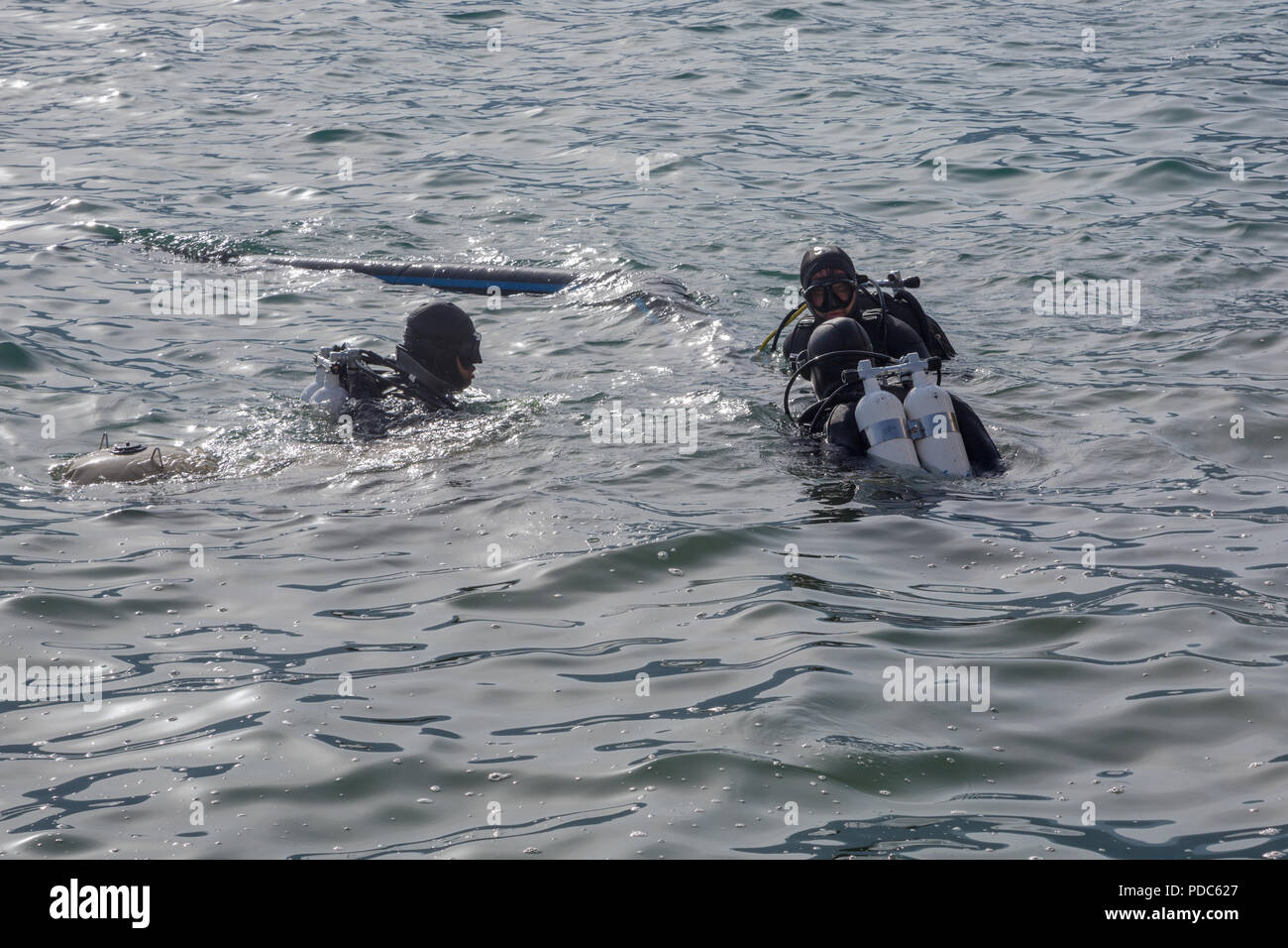 Three (3) male sub-aqua divers in black wetsuits with oxygen bottles swimming in sea with gentle surface waves in the Bay of Kotor, Perast, Montenegro Stock Photo